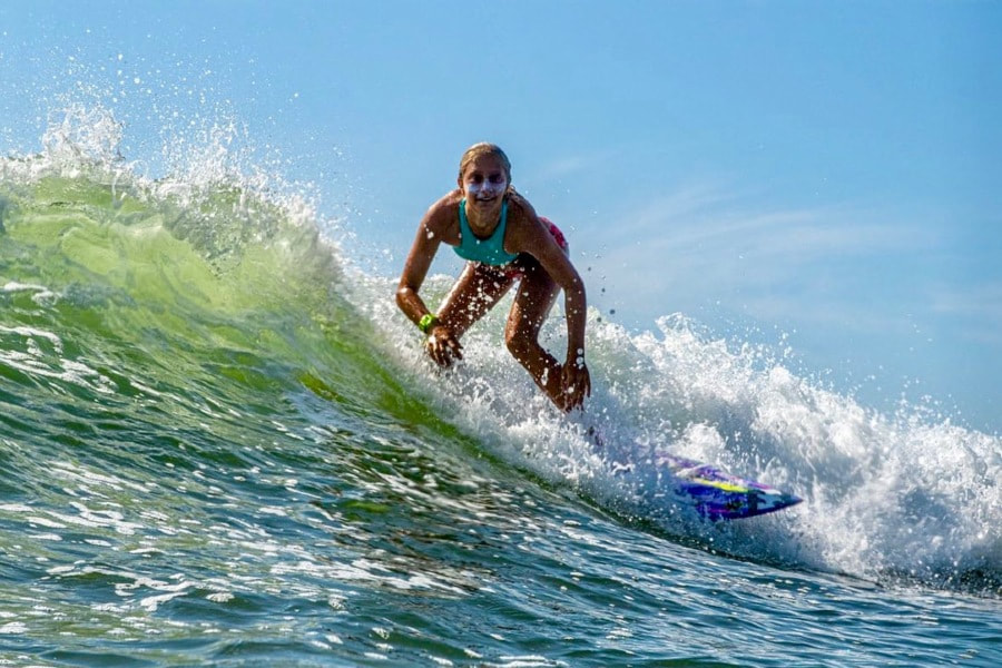 girl with suncreen on face smiles from surfboard